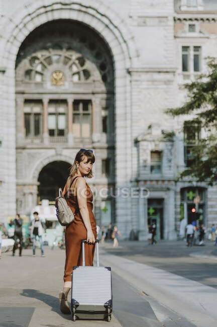 Молода жінка з валізою, що йде на вулиці — стокове фото