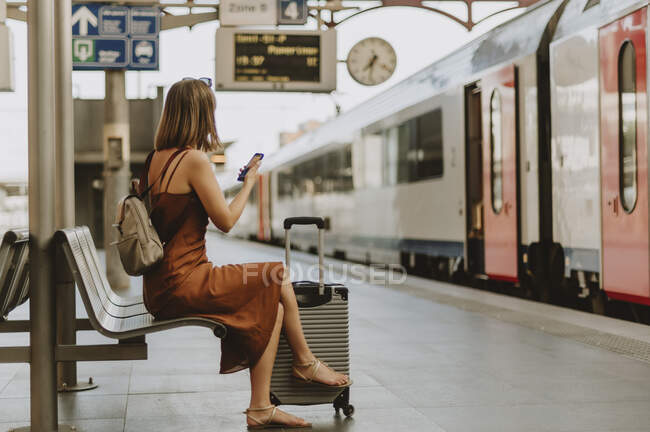 Young woman with backpack sitting on bench at railway station — Stock Photo