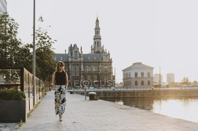 Молода жінка в чорній сукні з рюкзаком на фоні річки — стокове фото