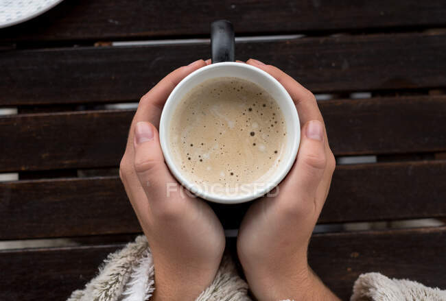 Mãos femininas segurando xícara de café quente, fundo de madeira — Fotografia de Stock