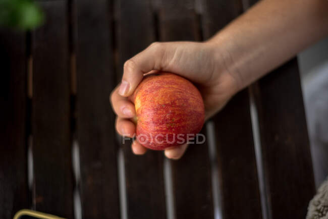 Рука, держащая красное яблоко и забор на заднем плане — стоковое фото