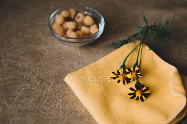 Yellow raspberries in a glass plate and marigolds on a napkin on a brown background — Stock Photo