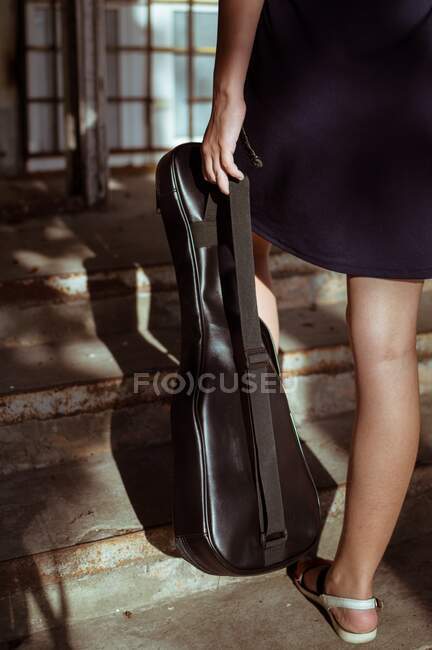 Los pies de una chica sosteniendo un estuche de guitarra en escalones vintage - foto de stock