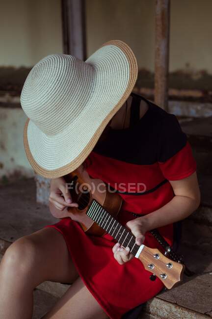 Side view of a sitting girl in a hat, playing the ukulele, on the old steps — Stock Photo