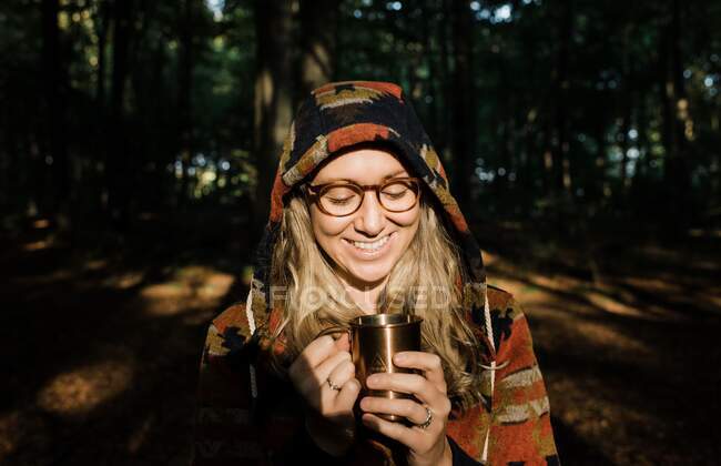 Молодая женщина с рюкзаком и чашкой кофе в лесу — стоковое фото