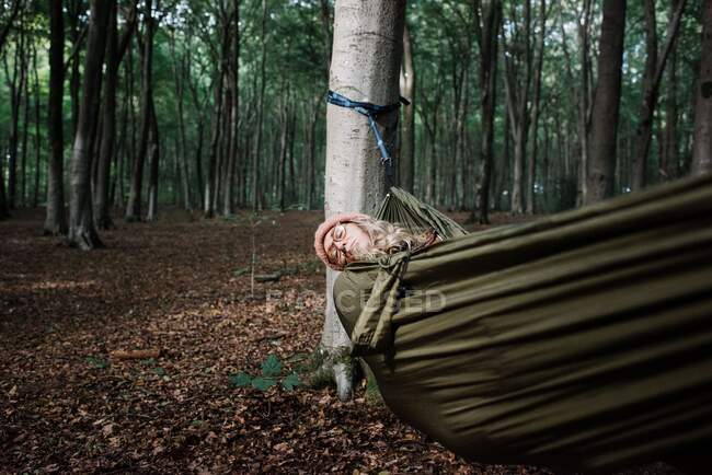 Una mujer hermosa está sentada en la hamaca en el bosque - foto de stock