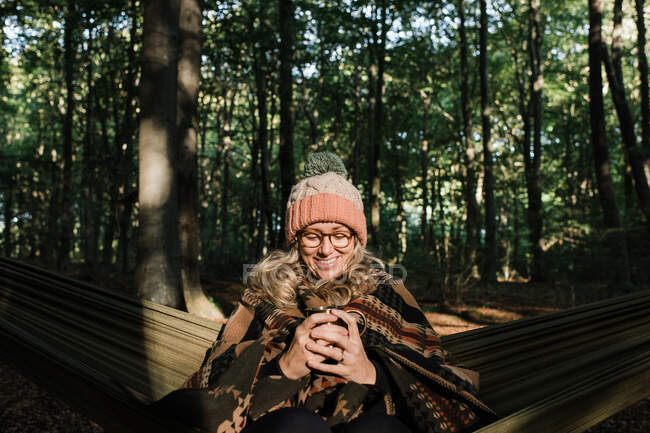 Frau mit Hut und Brille mit einer Tasse Kaffee im Wald. — Stockfoto