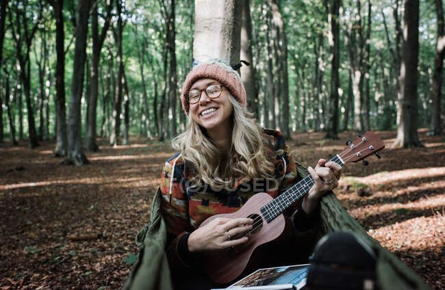 Jeune femme avec sac à dos et guitare en forêt — Photo de stock