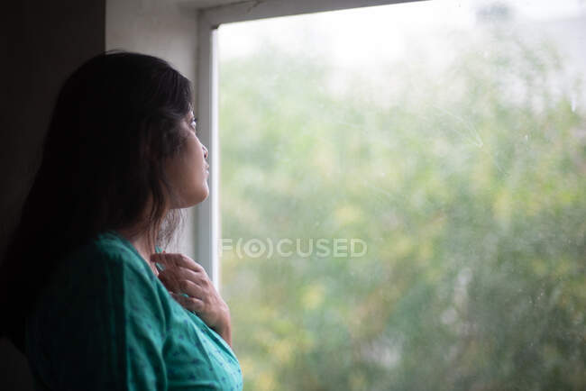 Jovem mulher vestindo vestido verde olhando para fora através da janela — Fotografia de Stock