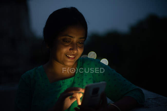 Молодая женщина смотрит на мобильный телефон на крыше в синий час — стоковое фото