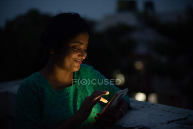 Jovem mulher olhando para celular no telhado em hora azul — Fotografia de Stock