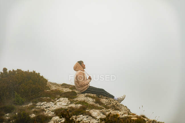 Niño sentado en una roca mirando hacia el horizonte - foto de stock