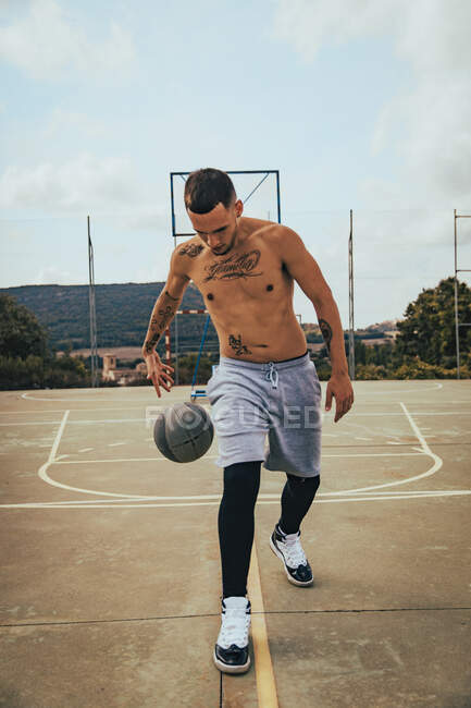 Jovem tatuado menino latino jogando com uma bola de basquete em uma quadra — Fotografia de Stock