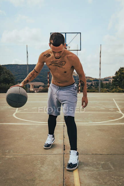 Jeune garçon latino tatoué jouant avec un basket sur un terrain — Photo de stock