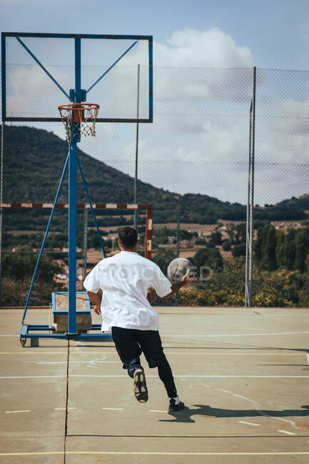 Jovem de costas jogando com um basquete em uma quadra — Fotografia de Stock
