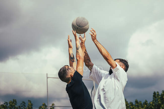 Dos amigos saltando en el aire mientras luchan contra un baloncesto - foto de stock