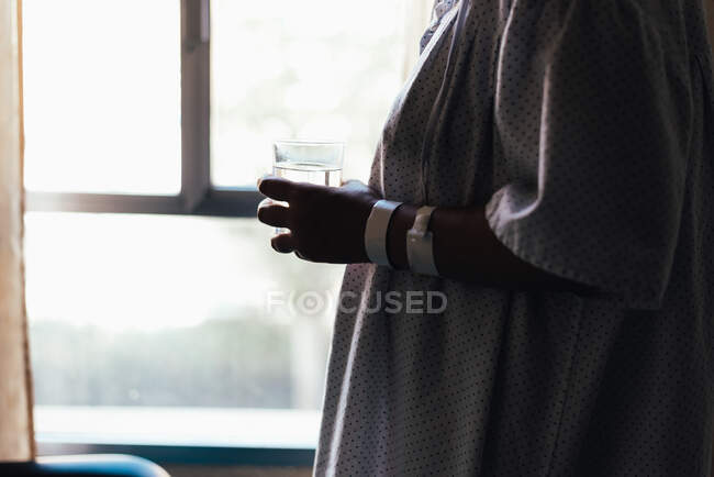 Крупный план больничного пациента, держащего стакан воды у окна. — стоковое фото