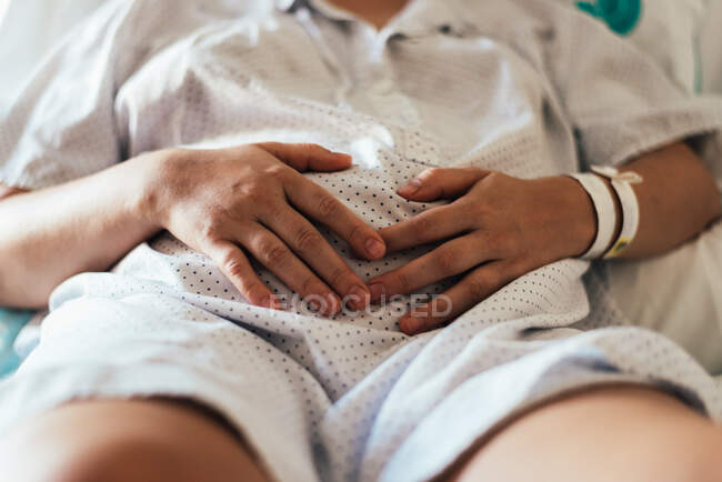 Young woman hospitalized in a bed. Gesture of pain in her belly. — Stock Photo