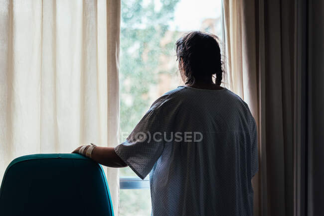 Un paciente joven mirando por la ventana de un hospital. - foto de stock