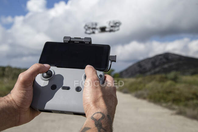 Las manos del hombre operando el control remoto del dron no tripulado mientras está parado en un camino de tierra - foto de stock