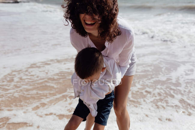 Joven hermosa mamá jugando con su hijo bebé en la playa - foto de stock
