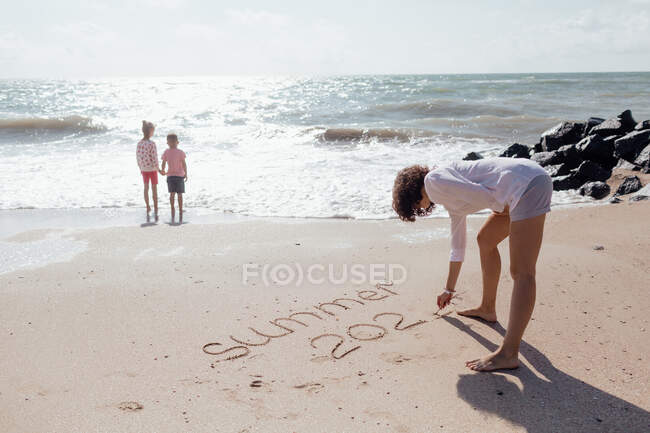 Молода красива матуся грає зі своїм маленьким сином і дівчинкою на пляжі — стокове фото
