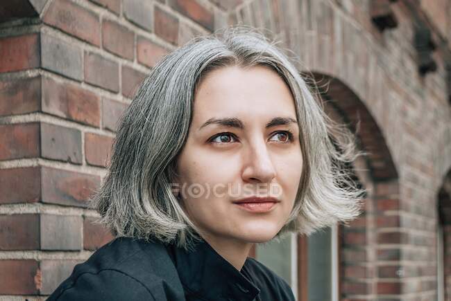 Eine grauhaarige Frau blickt vor dem Hintergrund eines Backsteingebäudes weg, ein Blick auf die nahe — Stockfoto