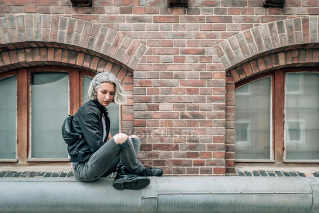 A woman sits in a Turkish pose on a pipe near an abandoned brick building — Stock Photo