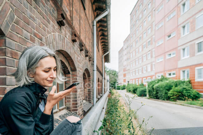 Una donna dai capelli grigi comunica su uno smartphone utilizzando messaggi vocali dall'esterno — Foto stock