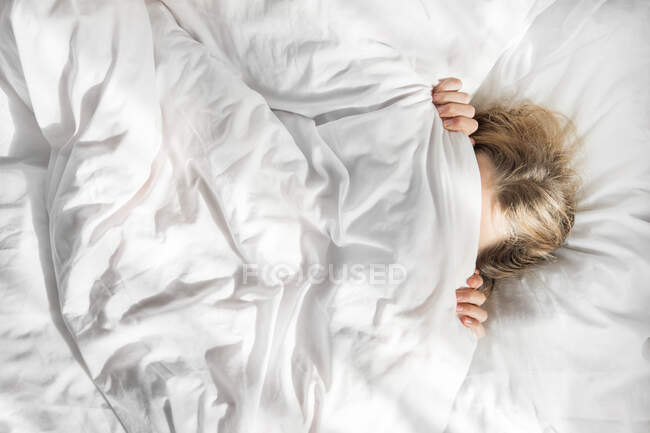 A menina se escondeu debaixo de um cobertor branco na cama — Fotografia de Stock
