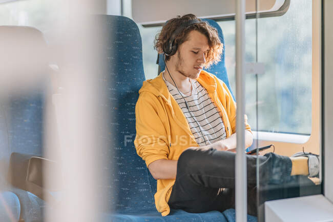 Молодой человек, подросток, путешествует в поезде в наушниках, слушает музыку. Снимок образа жизни с копированием пространства. — стоковое фото