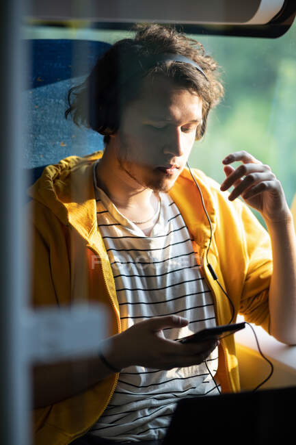 Молодий чоловік, підліток у навушниках, подорожує потягом, слухає музику по смартфонах. Стиль життя вертикальний постріл . — стокове фото