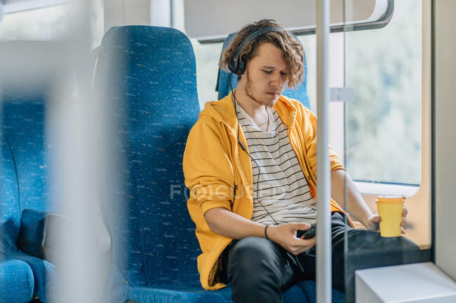 Jovem, adolescente, viajando de trem com fones de ouvido, bebe café, ouvindo música. Estilo de vida tiro com espaço de cópia. — Fotografia de Stock