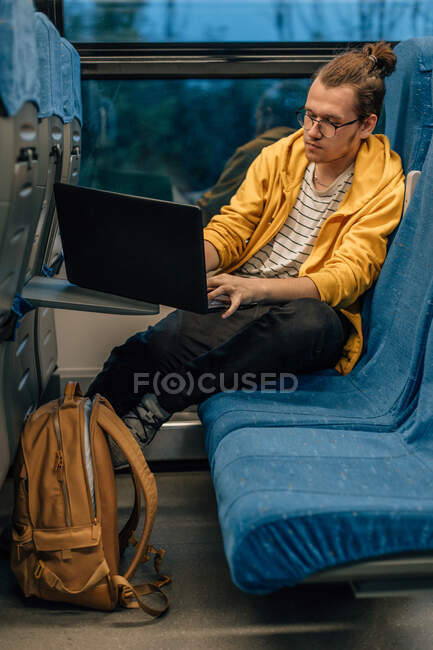 Junger Teenager mit Brille fährt im Zug mit Laptop, Programmierer arbeitet aus der Ferne. Vertikale Aufnahme, Porträt eines Reisenden. — Stockfoto