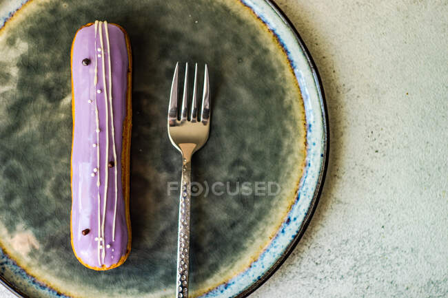 Tasty french dessert eclair with lavender topping on the plate — Stock Photo