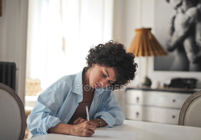 Young woman writes on paper with pen at home — Stock Photo
