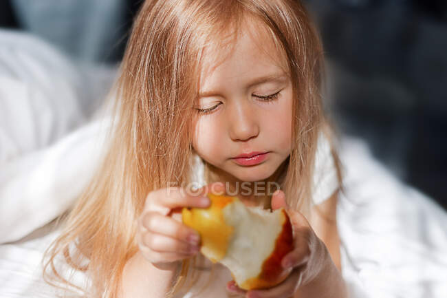 Сумна дівчина в сонячних променях їсть грушу в ліжку — стокове фото