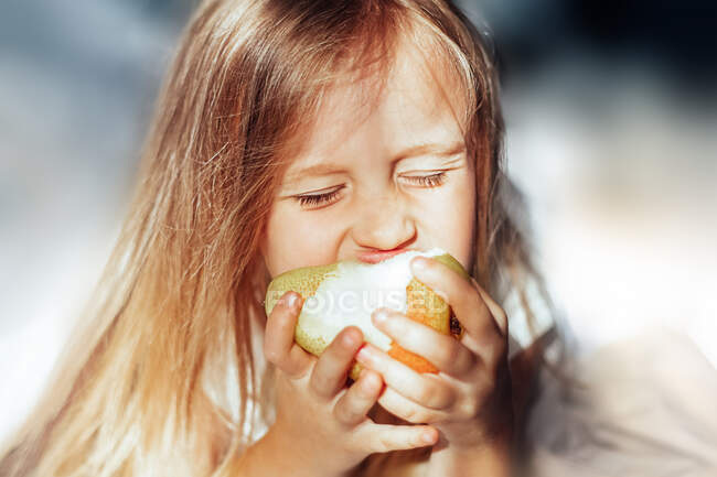 Mädchen am Morgen isst eine Birne im Bett — Stockfoto