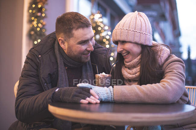 Casal romântico sentado à mesa no café ao ar livre e beber cacau durante o tempo de Natal — Fotografia de Stock