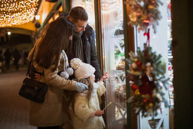 Promenade en famille et regardez la vitrine de la boutique avec des décorations de Noël pendant les vacances de Noël — Photo de stock