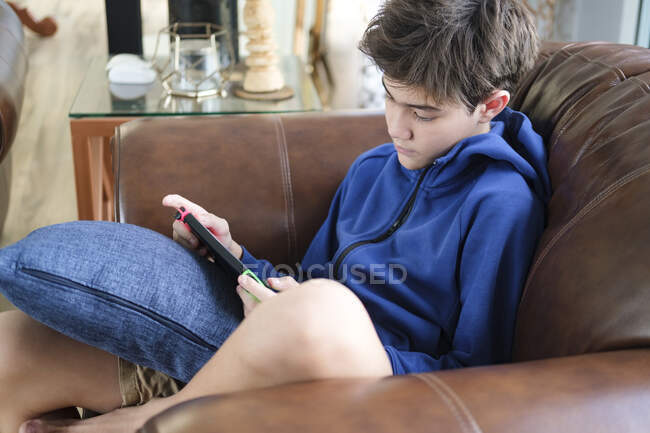 Хлопчик-підліток грає в гру на дивані у вітальні . — стокове фото