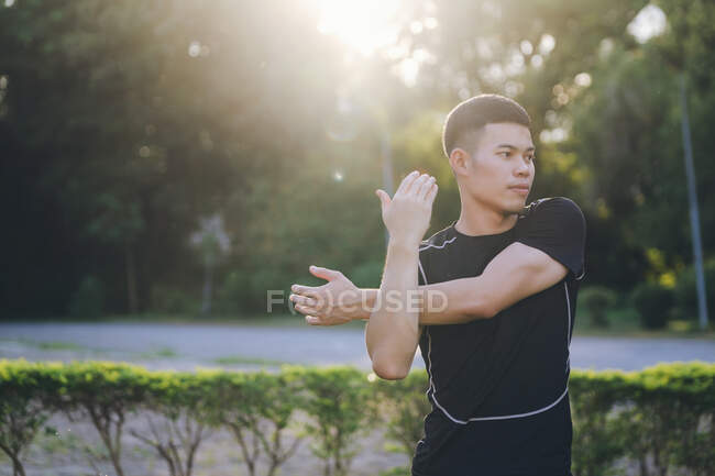 Jovem asiático masculino corredor aquecendo por alongamento braços e parte superior do corpo antes de correr. — Fotografia de Stock