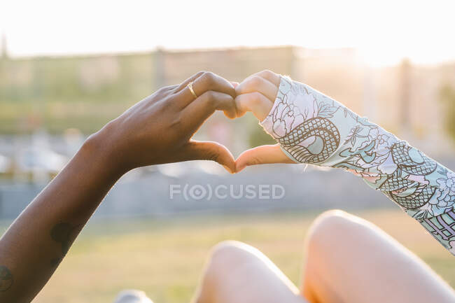 Crop multiracial girlfriends showing love gesture on meadow — Stock Photo