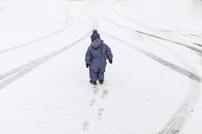 Маленький мальчик в синих ползунках выходит на улицу по снегу — стоковое фото