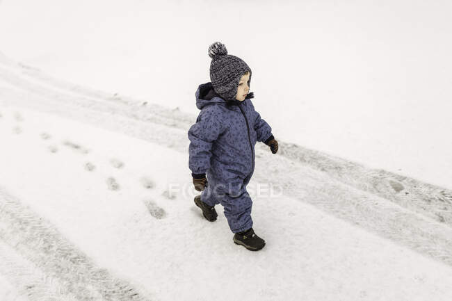 Маленький хлопчик у блакитних однокласниках впевнено виходить на вулицю на снігу — стокове фото