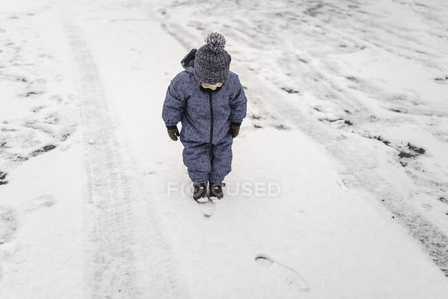 Little boy outside in warm blue onesie and hat looking at his fe — Stock Photo