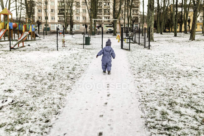 Petit garçon en bleu onesie et chapeau chaud va à aire de jeux — Photo de stock