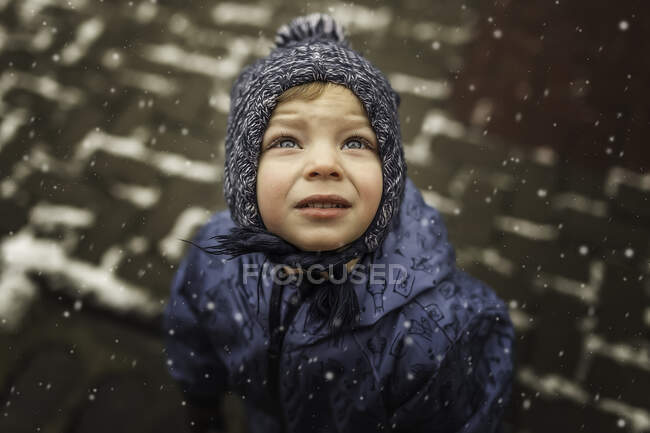 Menino pequeno em roupas azuis de inverno olhando para o céu nevando — Fotografia de Stock