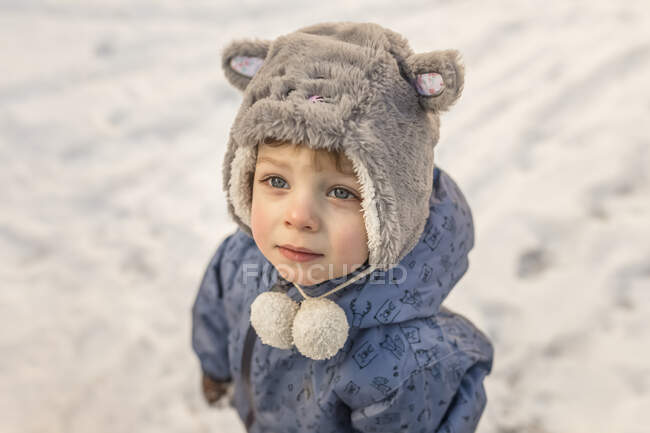 Small boy wearing furry grey hat and blue jacket standing on sno — Stock Photo