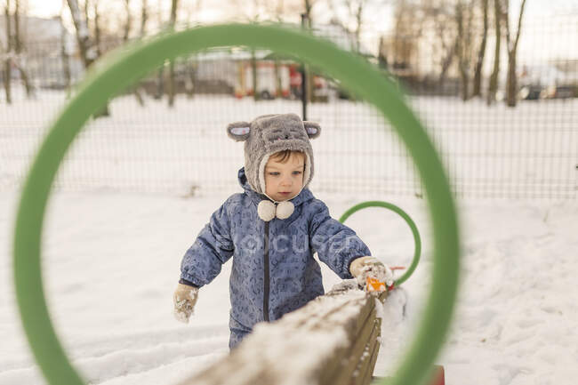 Niño en sombrero peludo gris y azul onesie jugando con la nieve en p - foto de stock